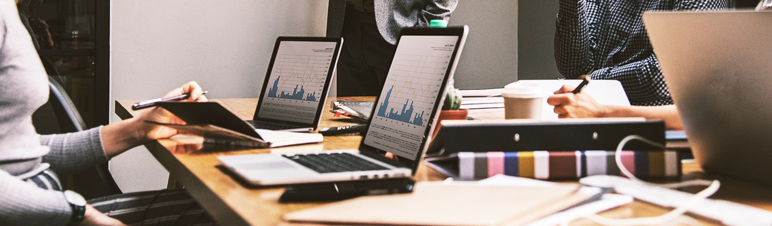 vier Personen arbeiten an einem Holztisch an Laptops, die Diagramme anzeigen, und Notizbüchern
