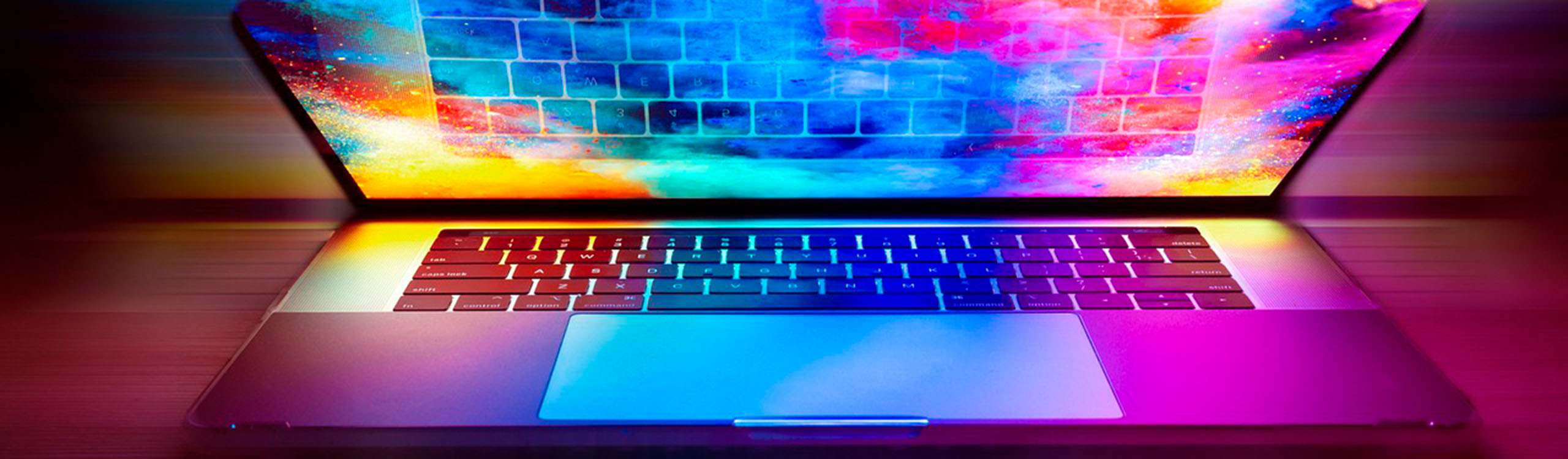 der Bildschirm eines aufgeschlagenes Laptop leuchtet in bunten Farben, die sich auf Tastatur und Gehäuse spiegeln
